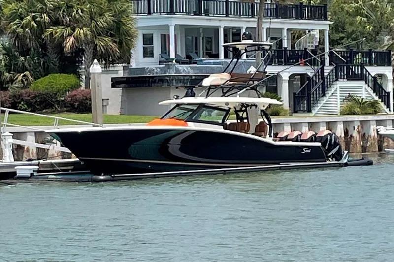 Slide: The Image of 2020 Scout 420 LXF boat docked by waterfront home, surrounded by lush greenery. - 2