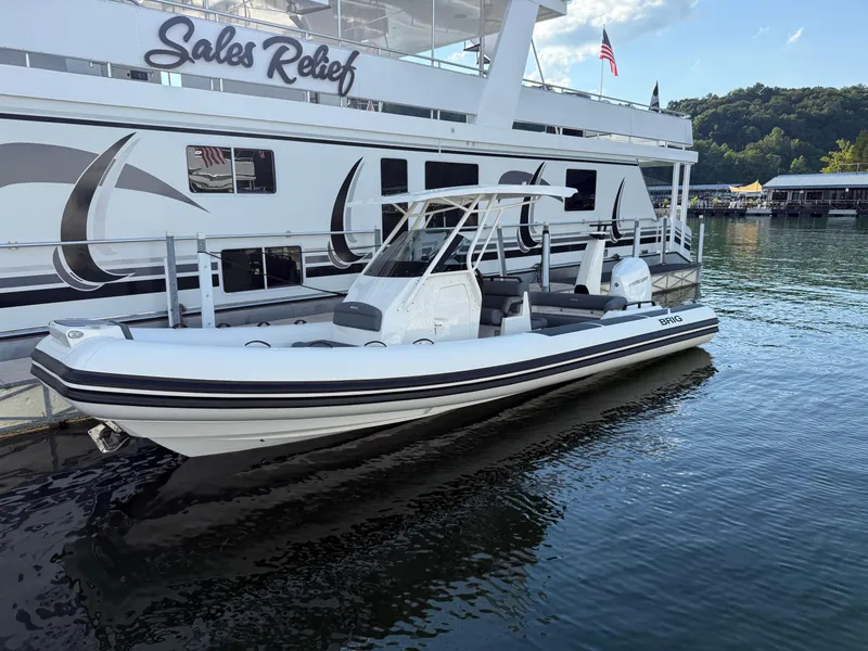 Slide: The Image of 2026 Brig Eagle 8 boat docked beside a large houseboat, with clear skies and calm water. - 32