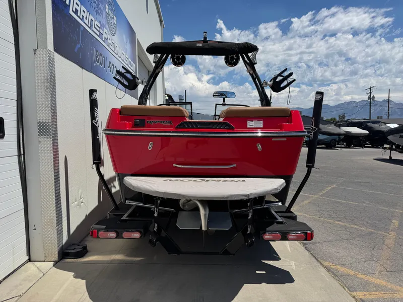 Slide: The Image of 2024 Moomba Craz boat, red exterior, parked outdoors at a marine dealership. - 2