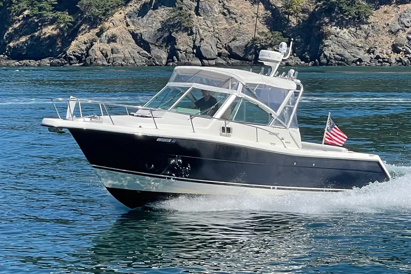 Slide: The Image of 2002 Pursuit 2860 Denali boat cruising on clear blue water near rocky shoreline. - 0