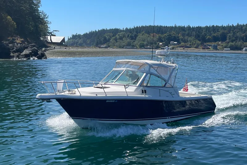 Slide: The Image of 2002 Pursuit 2860 Denali boat cruising on a scenic lake with forested shoreline. - 1