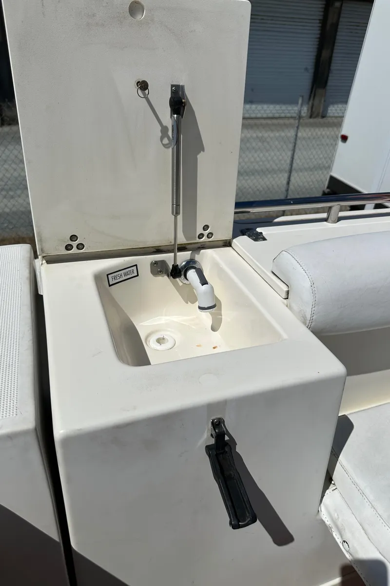 Slide: The Image of 2002 Pursuit 2860 Denali boat sink with fresh water tap, open lid, and white seating. - 16