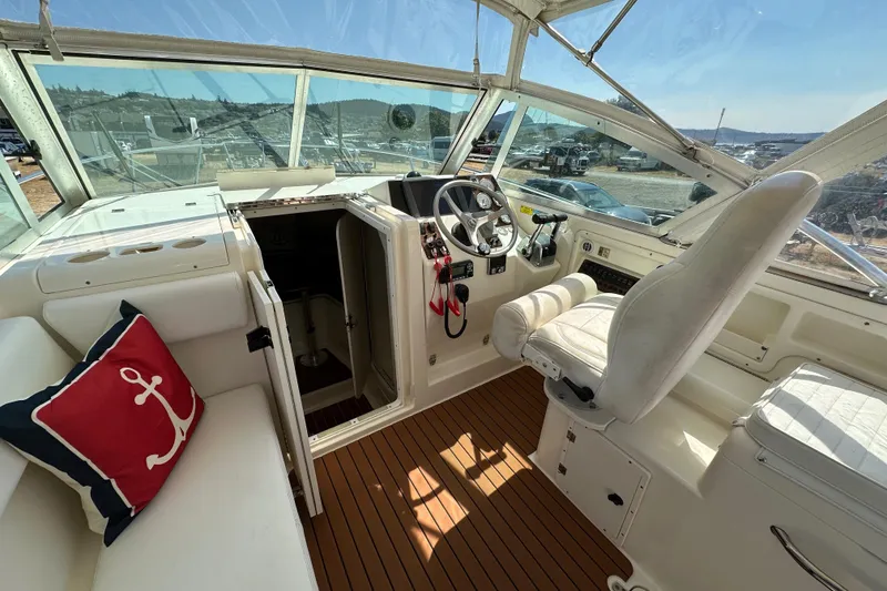 Slide: The Image of 2002 Pursuit 2860 Denali boat interior with helm, white seating, and nautical-themed pillow. - 18