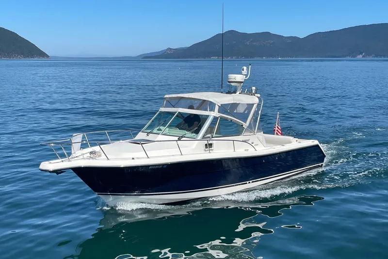 Slide: The Image of 2002 Pursuit 2860 Denali boat cruising on clear blue water with scenic mountain backdrop. - 3