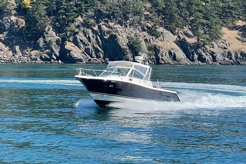 Slide: The Image of 2002 Pursuit 2860 Denali boat cruising on clear blue water near rocky shoreline. - 55