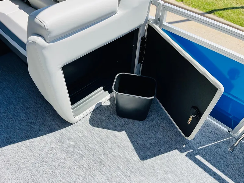 Slide: The Image of 2026 Sun Tracker Fishin' Barge 20 DLX storage compartment with open door and trash bin. - 25