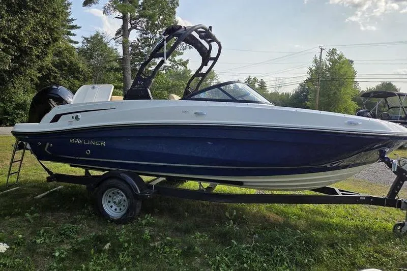 Slide: The Image of 2025 Bayliner VR5 OB boat on trailer, parked on grass with trees in background. - 10