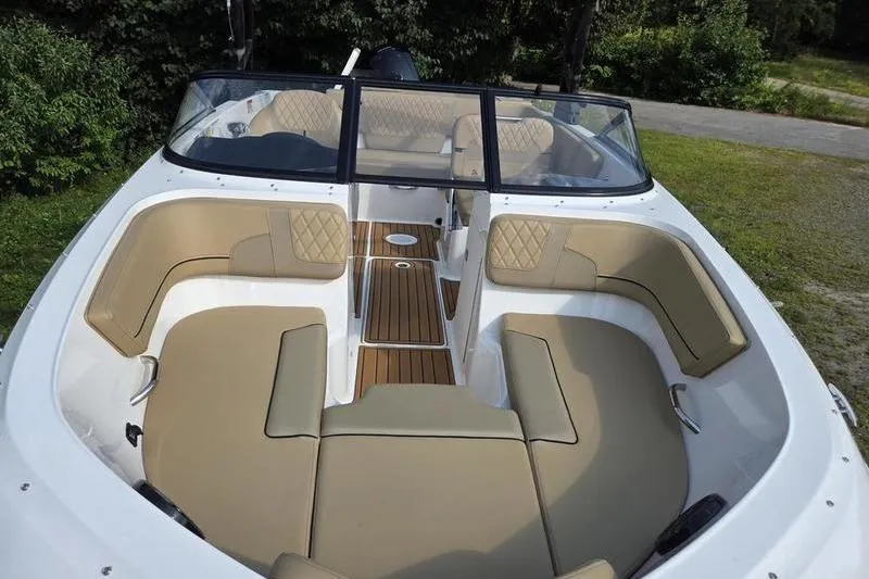 Slide: The Image of 2025 Bayliner VR5 OB boat with tan seating and wood flooring, parked on grass. - 4