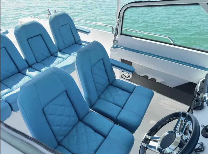 Slide: The Image of 2020 Axopar 28 TT boat interior with blue seating and steering wheel, on calm water. - 11