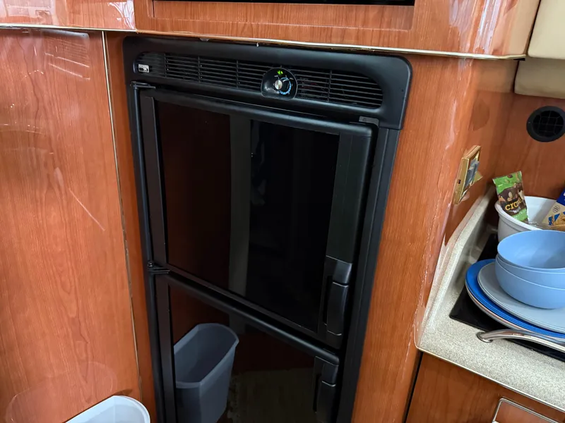 Slide: The Image of 1999 Sea Ray 400 Sedan Bridge interior with a compact black refrigerator and wooden cabinetry. - 27
