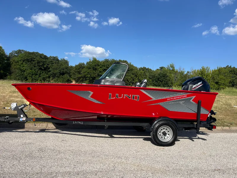 Slide: The Image of 2024 Lund 1675 Adventure Sport boat in vibrant red on a trailer, outdoors. - 2
