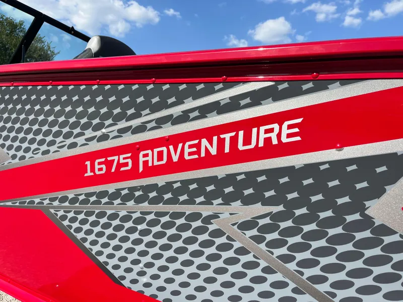 Slide: The Image of 2024 Lund 1675 Adventure Sport boat with red and gray design under blue sky. - 31