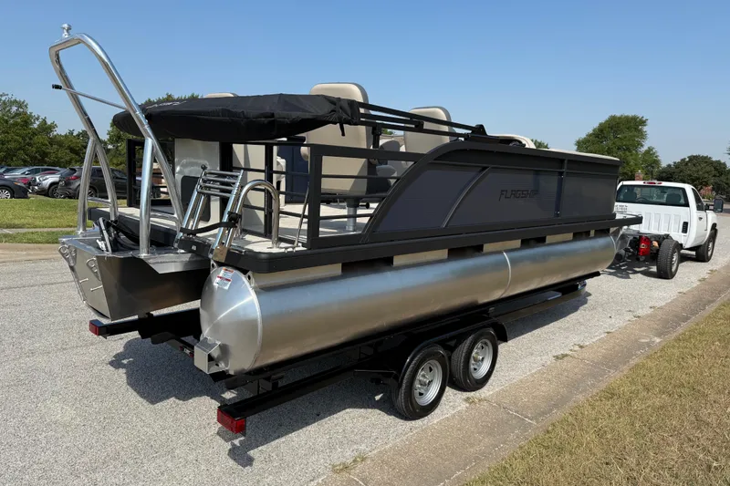 Slide: The Image of 2025 Flagship E22RF Sport Toon pontoon boat on trailer, parked outdoors. - 16