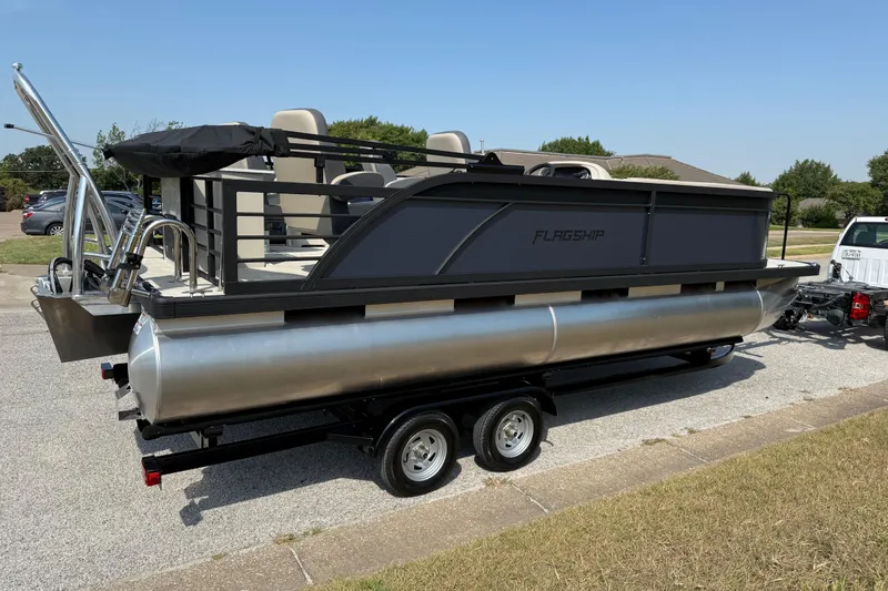 Slide: The Image of 2025 Flagship E22RF Sport Toon pontoon boat on trailer, parked outdoors. - 17