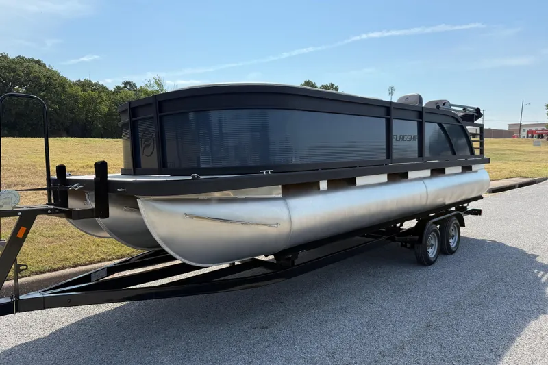 Slide: The Image of 2025 Flagship E22RF Sport Toon pontoon boat on a trailer, parked on a sunny day. - 2
