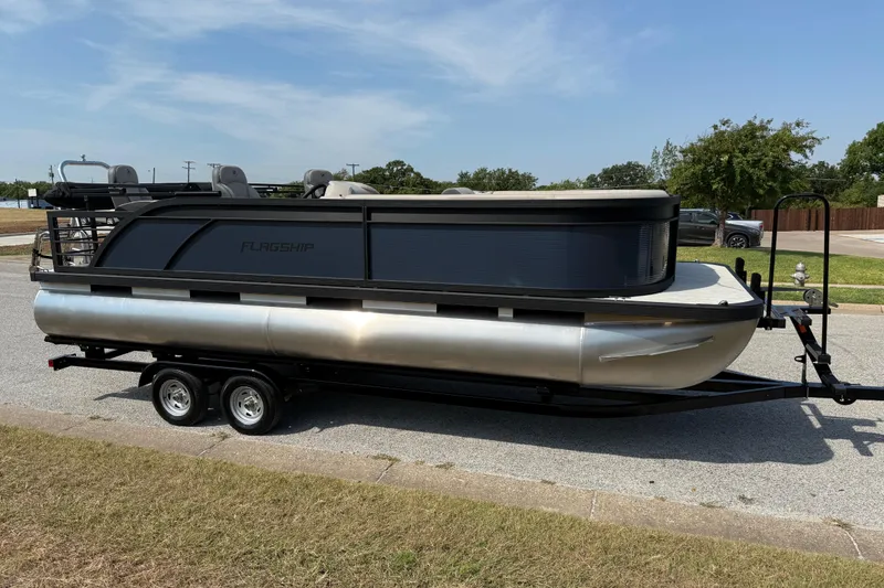 Slide: The Image of 2025 Flagship E22RF Sport Toon pontoon boat on a trailer, parked outdoors. - 20