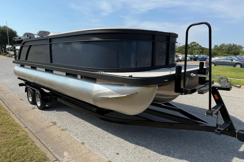 Slide: The Image of 2025 Flagship E22RF Sport Toon pontoon boat on trailer, parked on a street. - 22