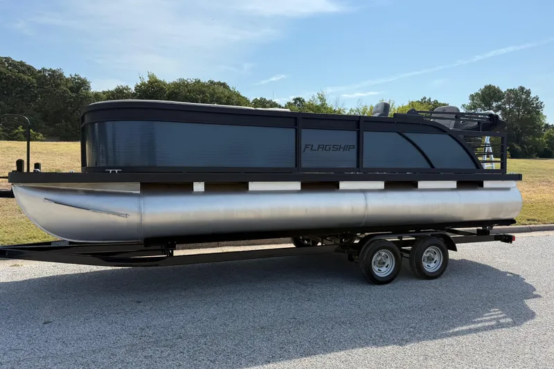 Slide: The Image of 2025 Flagship E22RF Sport Toon pontoon boat on trailer, parked outdoors. - 3