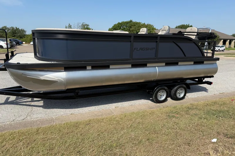 Slide: The Image of 2025 Flagship E22RF Sport Toon pontoon boat on trailer, parked outdoors. - 36