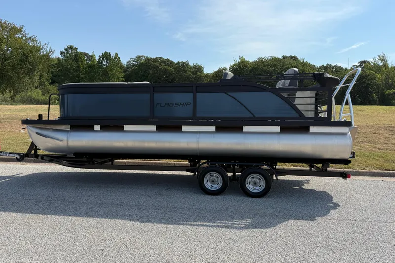 Slide: The Image of 2025 Flagship E22RF Sport Toon pontoon boat on trailer, parked outdoors. - 4