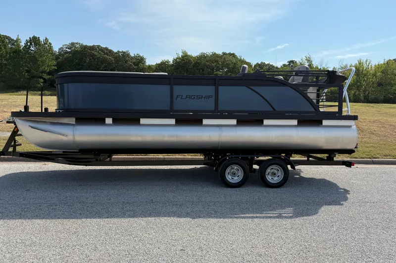 Slide: The Image of 2025 Flagship E22RF Sport Toon pontoon boat on trailer, parked on a sunny day. - 7