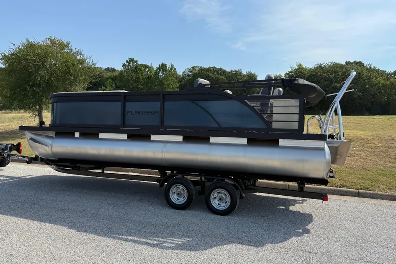 Slide: The Image of 2025 Flagship E22RF Sport Toon pontoon boat on trailer, parked outdoors. - 8