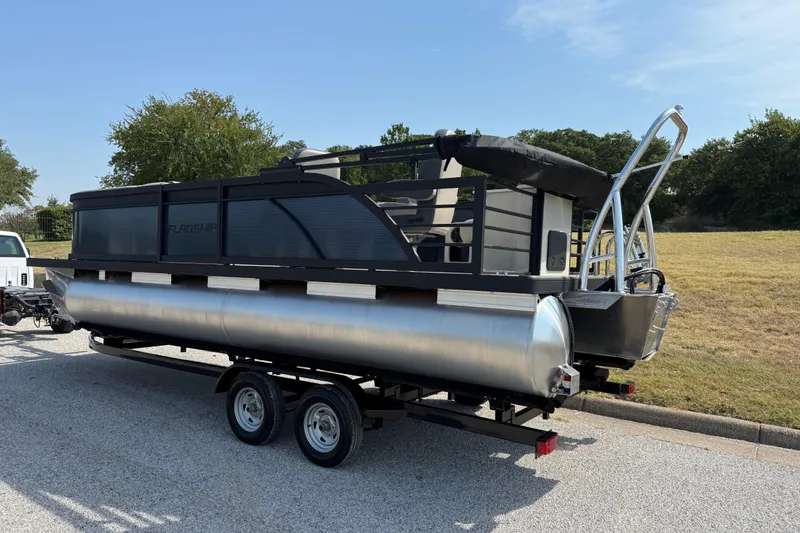 Slide: The Image of 2025 Flagship E22RF Sport Toon pontoon boat on trailer, parked outdoors. - 9