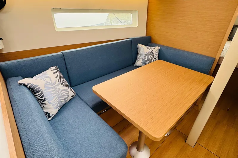 Slide: The Image of 2023 Jeanneau 380 interior with blue seating, wooden table, and decorative pillows. - 49