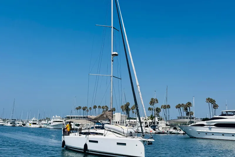 Slide: The Image of 2023 Jeanneau 380 sailboat in marina, clear blue sky, palm trees in background. - 69