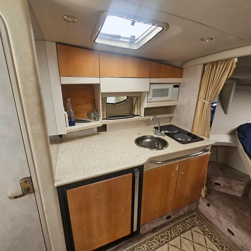 Slide: The Image of Compact kitchen area in a 2000 Formula 31 PC boat, featuring wood cabinets and modern appliances. - 17