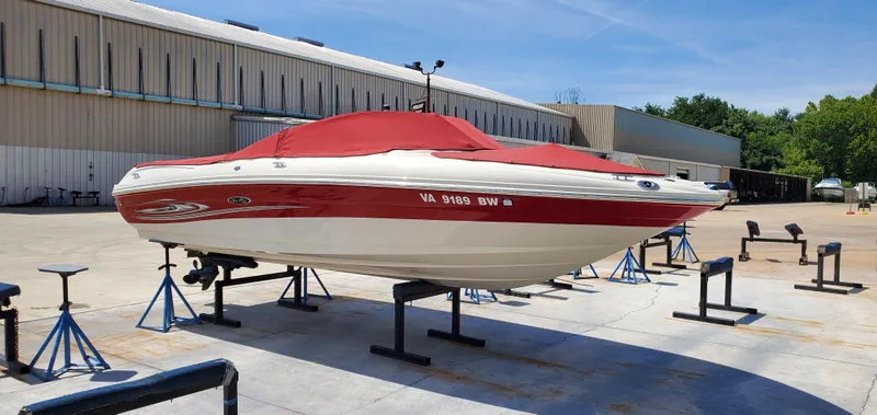 The Image of 2005 Sea Ray 200 Sport boat with red cover on stands in a marina. - 0