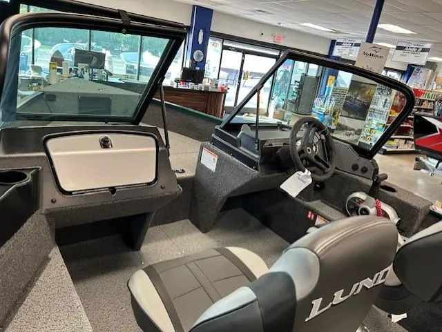 Slide: The Image of 2026 Lund 1650 Angler Sport boat interior with steering wheel and seating in showroom. - 3