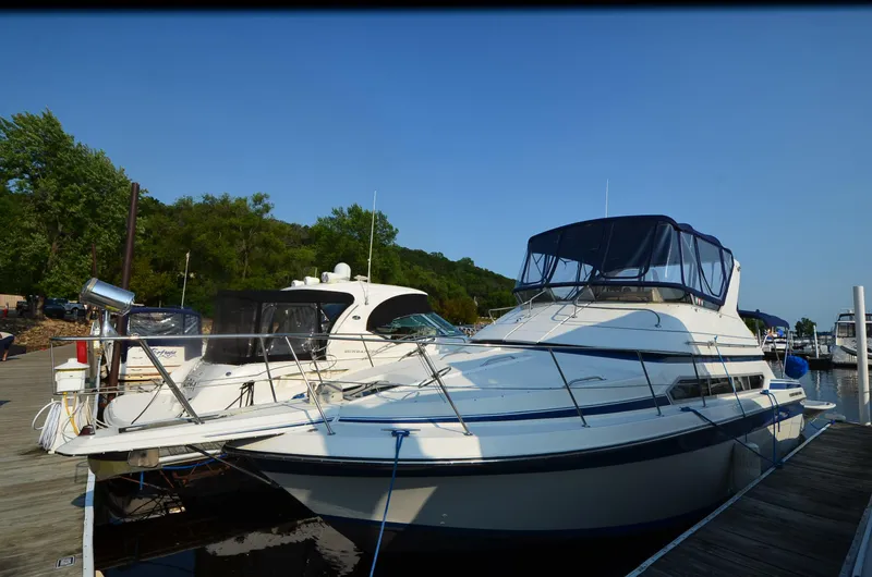 The Image of 1989 Carver SANTEGO yacht docked at a marina, surrounded by trees and clear blue sky. - 1