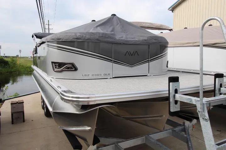 Slide: The Image of 2025 Avalon LSZ Quad Lounger Shift pontoon boat with cover, docked near a building. - 3