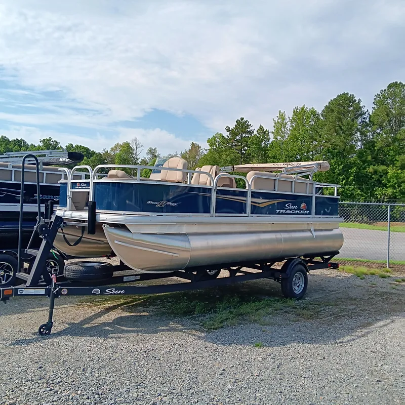 Slide: The Image of 2025 Sun Tracker Bass Buggy 18 DLX pontoon boat on trailer, parked outdoors. - 2