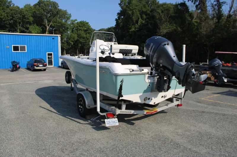 Slide: The Image of 2021 Tidewater 198 CC Adventure boat on trailer, parked near a blue building. - 5