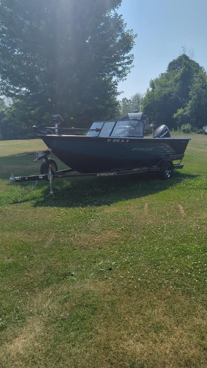 Slide: The Image of 2019 Starcraft Titan 186 boat on trailer, parked on grassy area with trees in background. - 13