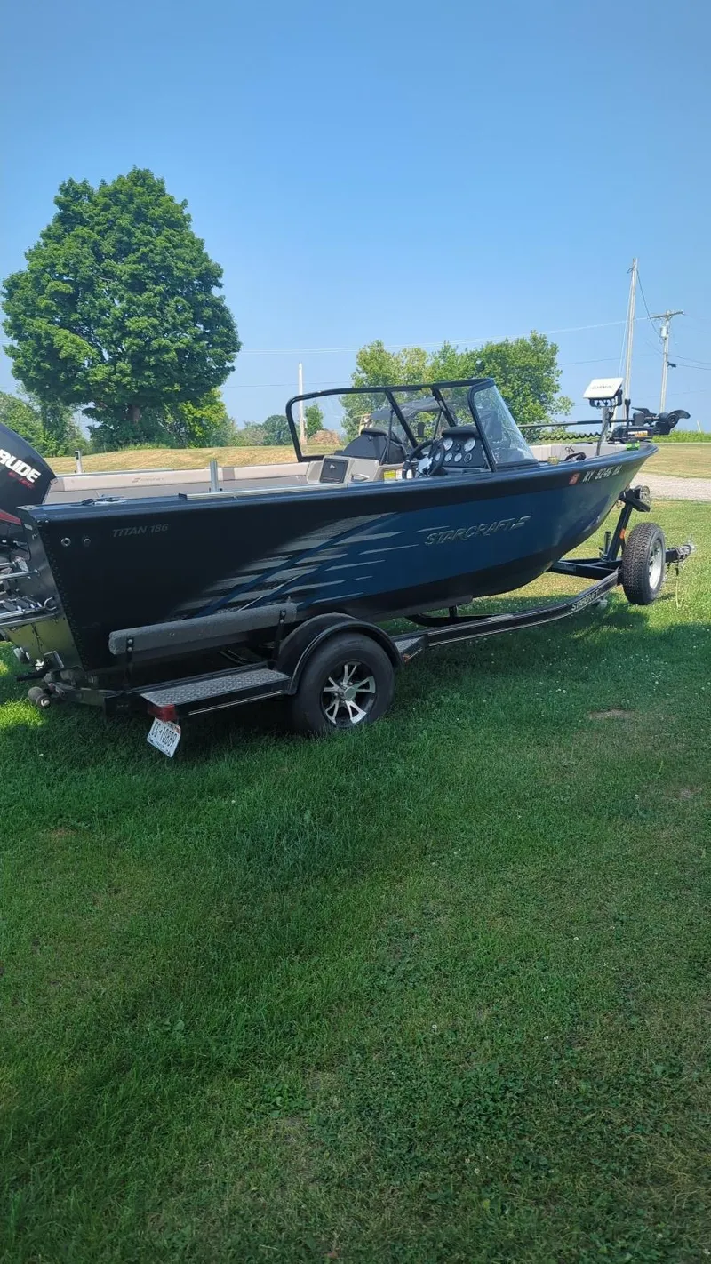 Slide: The Image of 2019 Starcraft Titan 186 boat on trailer, parked on grass under clear blue sky. - 14