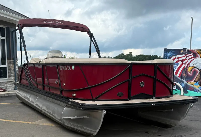 Slide: The Image of 2018 South Bay 523CR pontoon boat with red exterior, parked near a mural and building. - 0