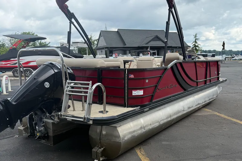 Slide: The Image of 2018 South Bay 523CR pontoon boat with red exterior and outboard motor, parked on pavement. - 1