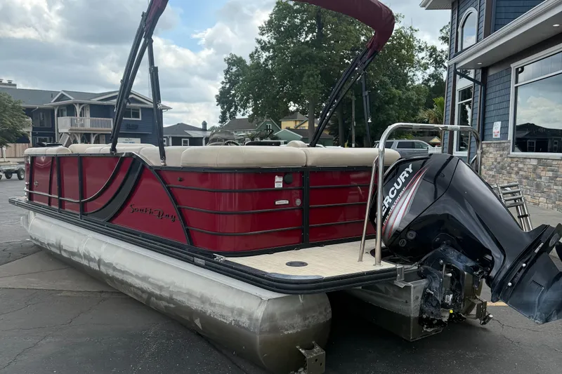 Slide: The Image of 2018 South Bay 523CR pontoon boat with Mercury outboard motor, parked near buildings. - 2