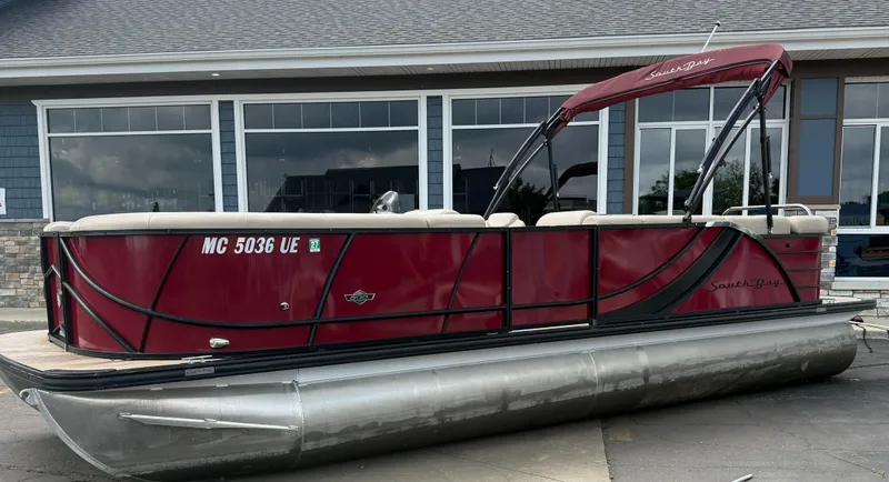 Slide: The Image of 2018 South Bay 523CR pontoon boat with maroon exterior, parked outside a building. - 3