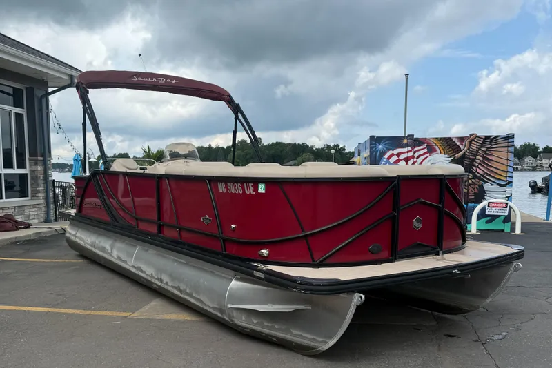 Slide: The Image of 2018 South Bay 523CR pontoon boat docked near a lakeside building under cloudy skies. - 5
