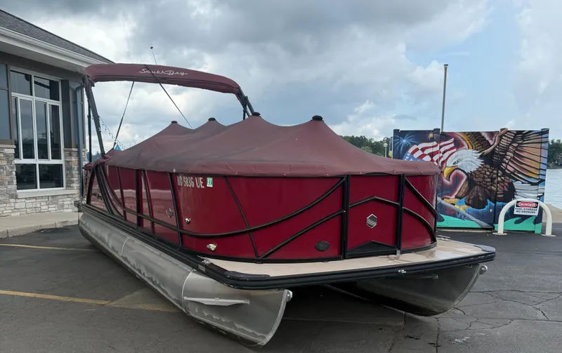 Slide: The Image of 2018 South Bay 523CR pontoon boat with maroon cover, parked near a mural and building. - 7