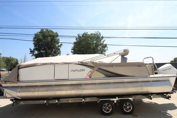 Slide: The Image of 2025 Avalon LSZ Versatile Rear Bench pontoon boat on trailer, covered, outdoors. - 13