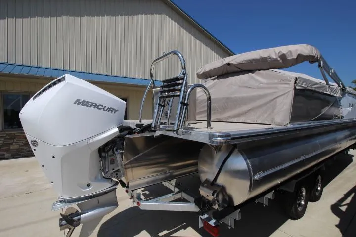 Slide: The Image of 2025 Avalon LSZ Versatile Rear Bench pontoon boat with Mercury outboard motor, parked outdoors. - 2