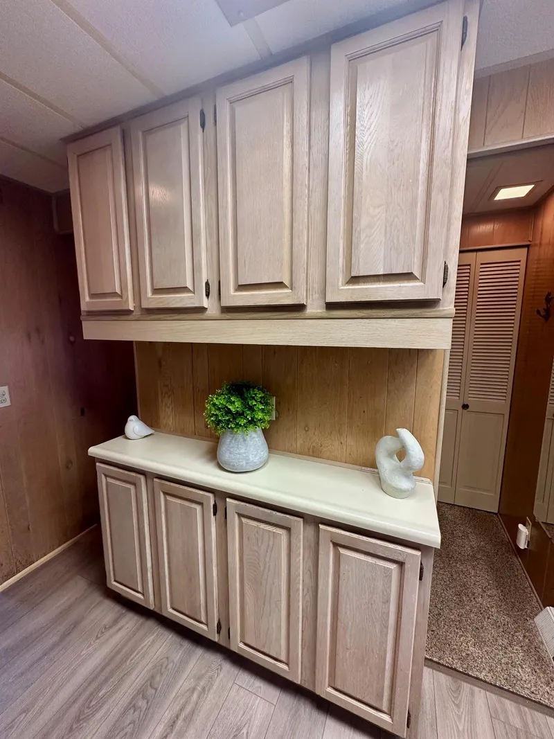 Slide: The Image of Wooden cabinets in a 1992 Sumerset 14x66 houseboat interior, featuring decorative plants and sculptures. - 6