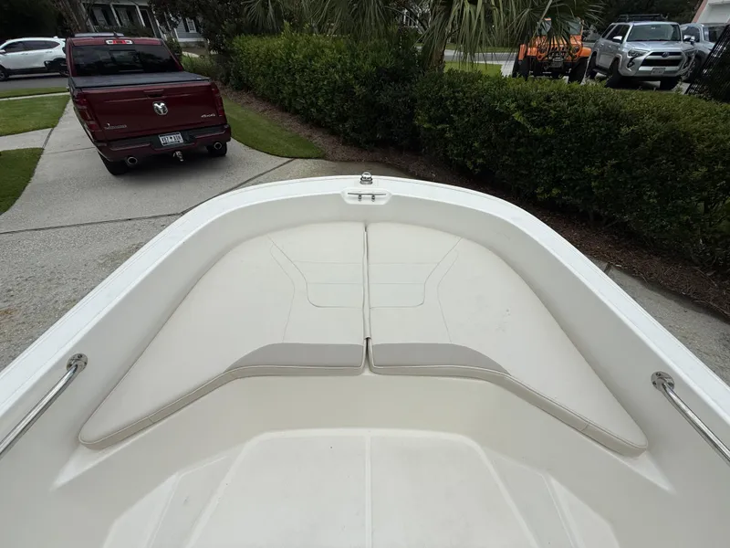 Slide: The Image of 2022 Boston Whaler 160 Super Sport boat interior with cushioned seating, parked near a red truck. - 13