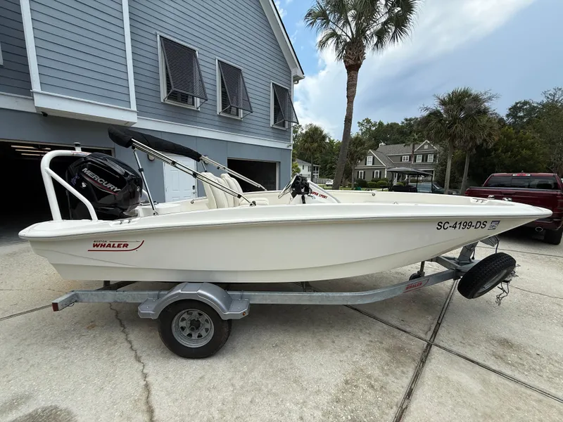 Slide: The Image of 2022 Boston Whaler 160 Super Sport boat on trailer, parked near a house. - 2