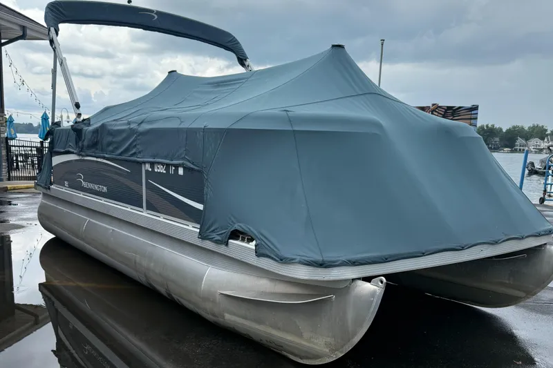 Slide: The Image of 2009 Bennington 1850GL pontoon boat with cover, docked by a lake under cloudy skies. - 10